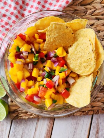 mango pico de gallo - mango chili salsa - in glass bowl with limes