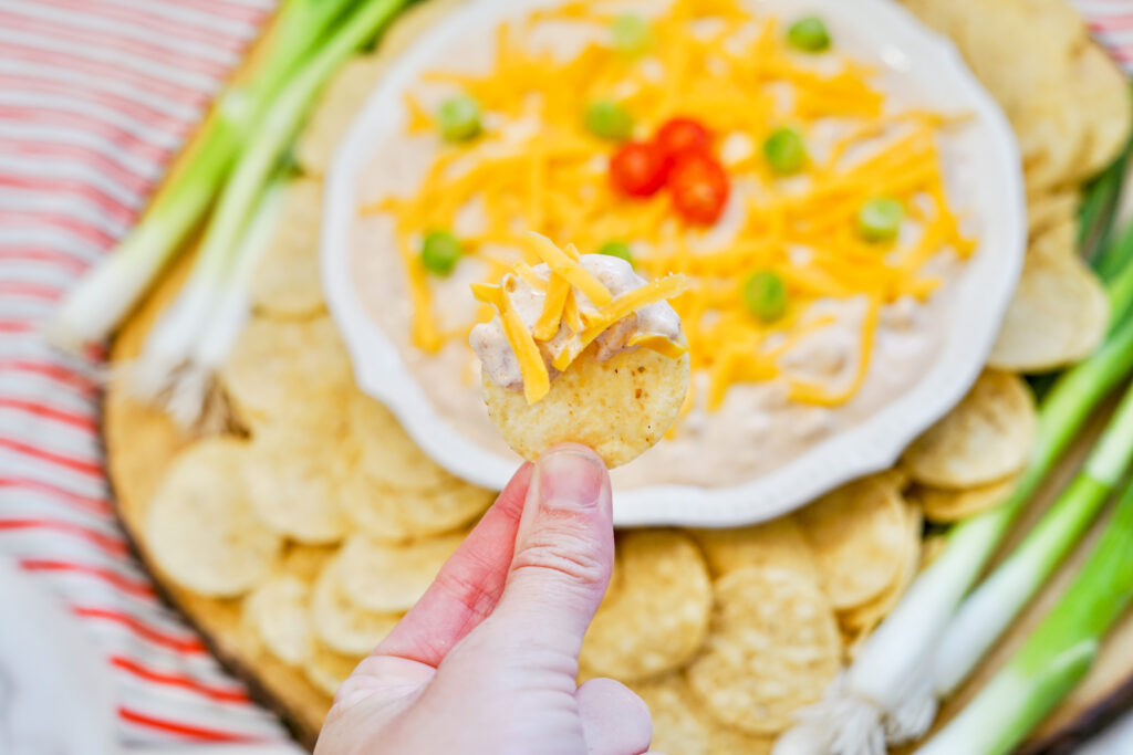 woman holds chip with TikTok boat dip - sour cream taco seasoning dip - in hand over bowl