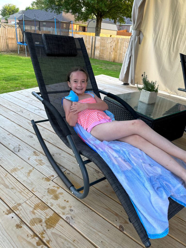 little girl lounging on an outdoor patio chaise rocker by the pool 