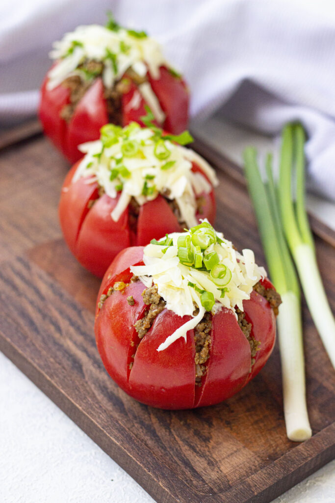 three stuffed taco tomatoes on wooden board with green onion beside