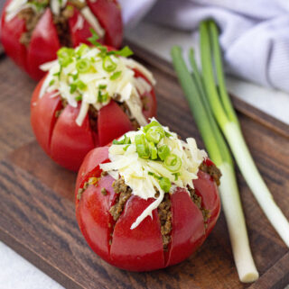 taco stuffed tomatoes on brown tray with green onions to the right
