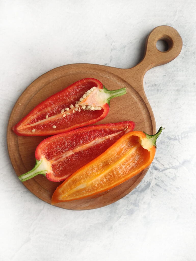 long thin bell peppers sliced in half on wooden board