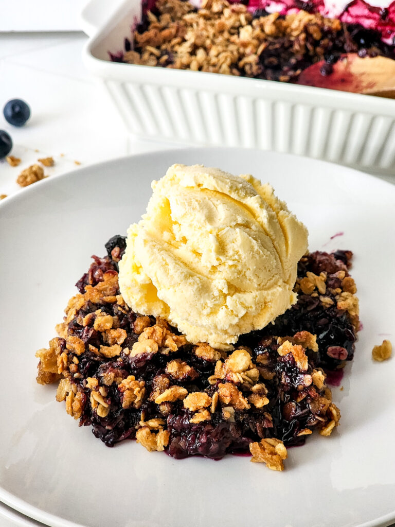 blueberry crisp with granola and vanilla ice cream on a white plate