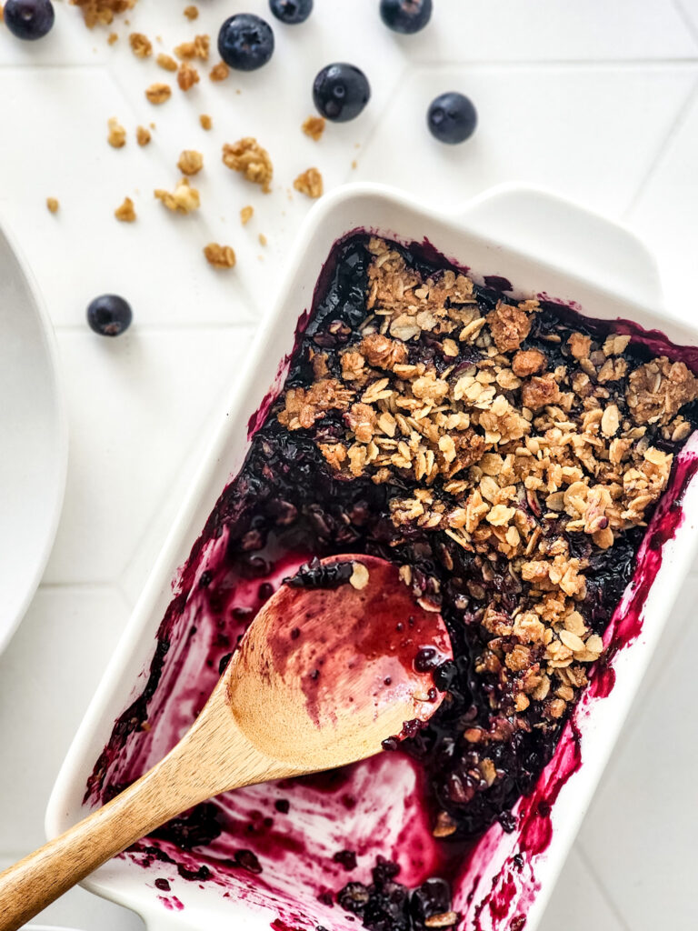 serving pan of blueberry crisp with granola and a wooden spoon