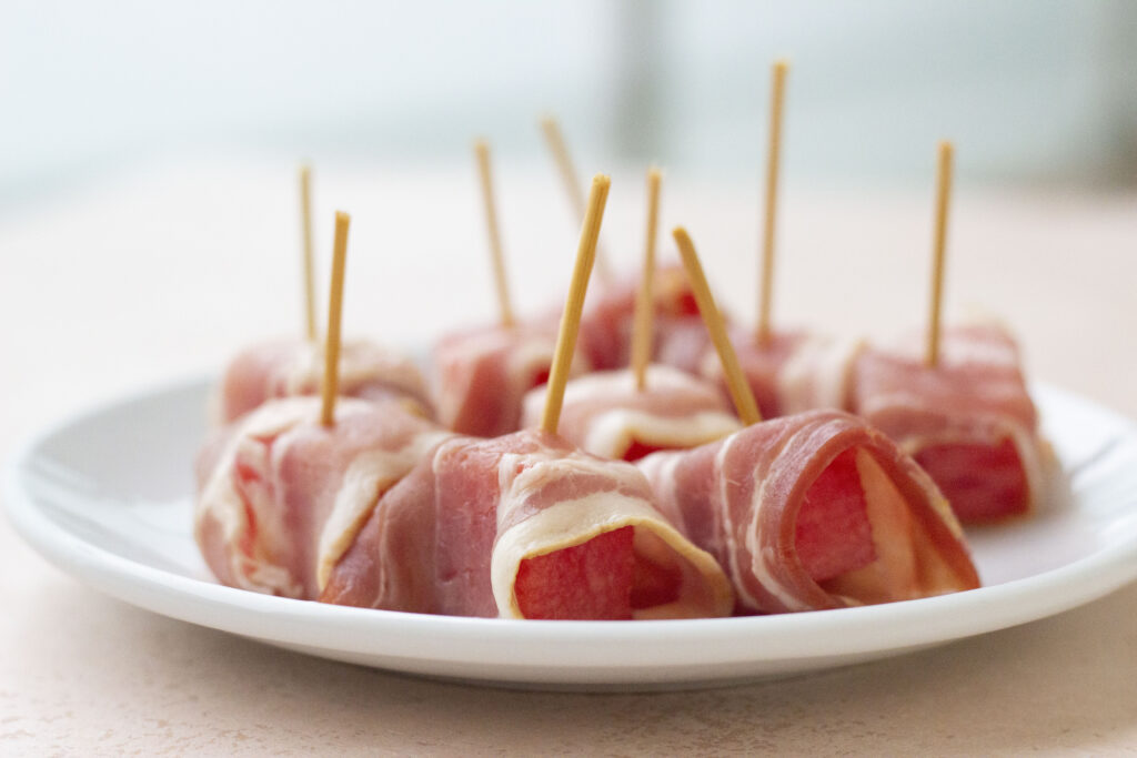 bacon wrapped watermelon uncooked on plate with toothpicks in top
