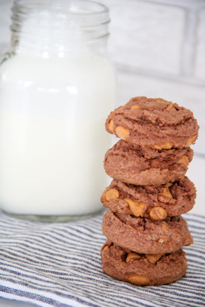 tall stack of chocolate pudding cookies with butterscotch chips beside pitcher of milk