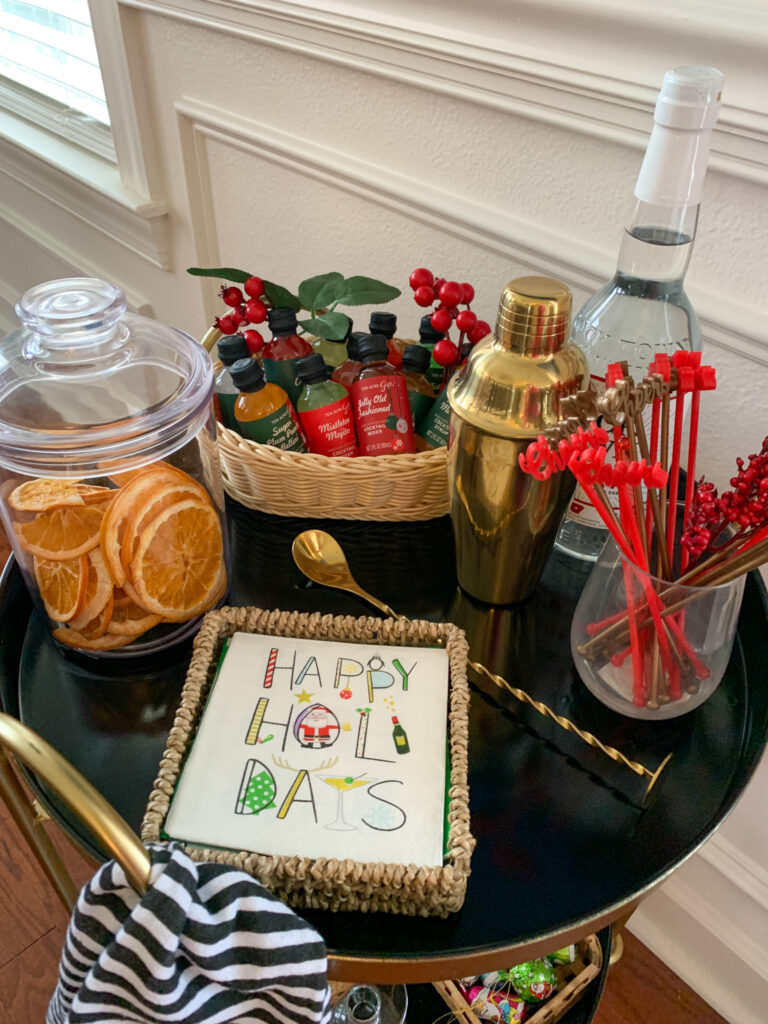 Christmas bar cart top shelf with holidays napkins, Christmas swizzle sticks, and more