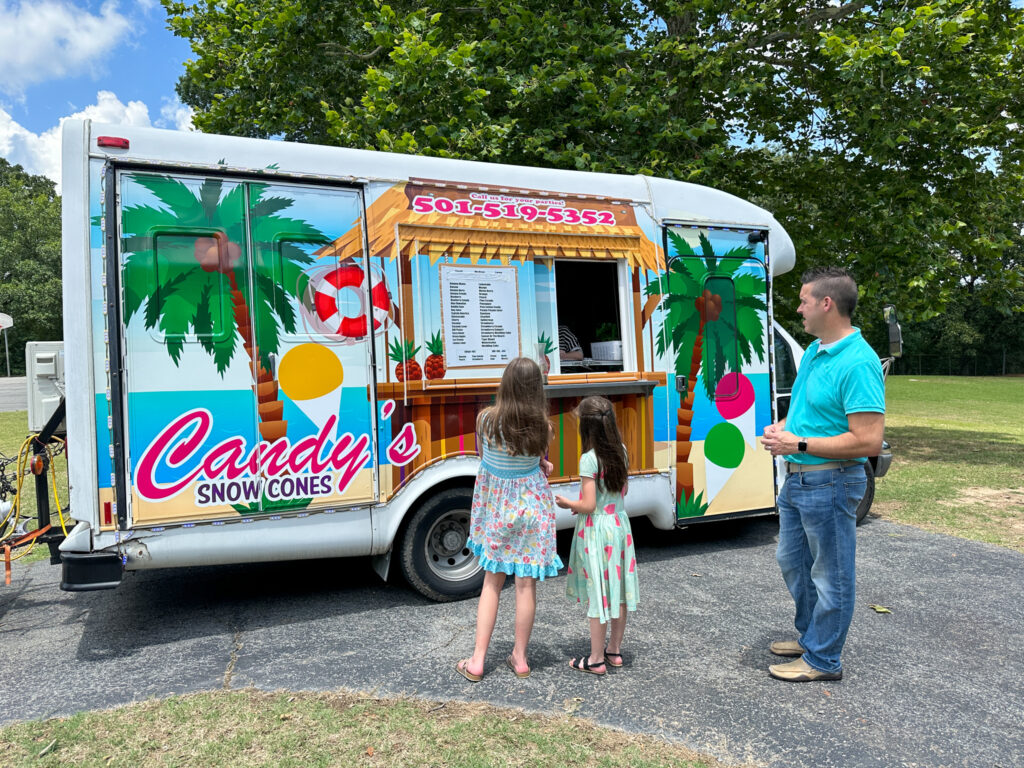 man and two children in front of Candy's Snow Cones truck at Sherwood Forest as part of company picnic ideas