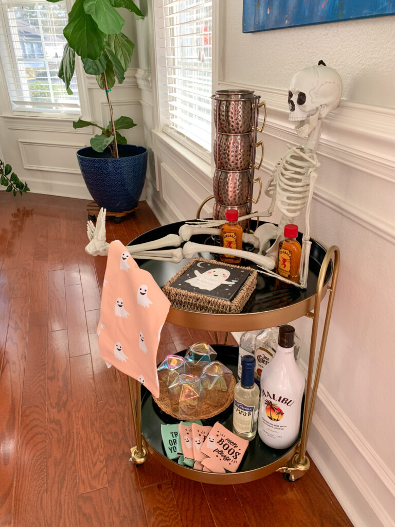 ghost decor and liquor on a Halloween bar cart with a small skeleton