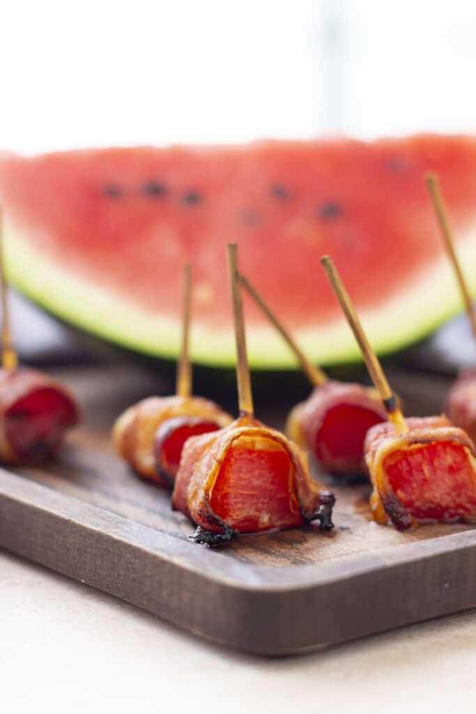 chunks of watermelon wrapped in bacon on wood cutting board