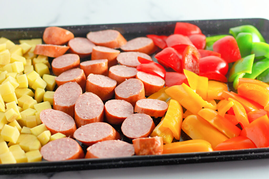 sheet pan full of uncooked kielbasa sausage, veggies and potatoes
