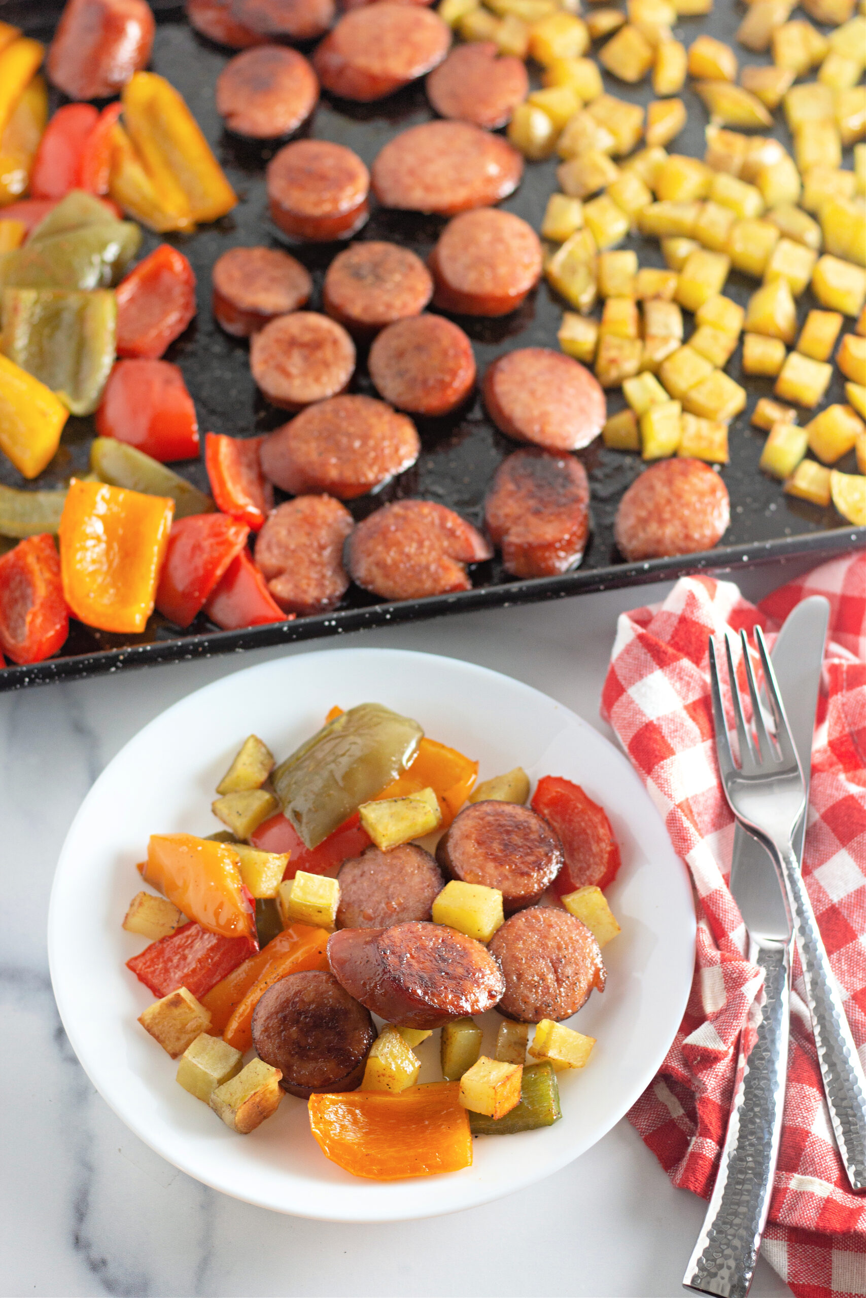 plate with kielbasa potato pepper bake with kielbasa sheet pan meal in pan at back