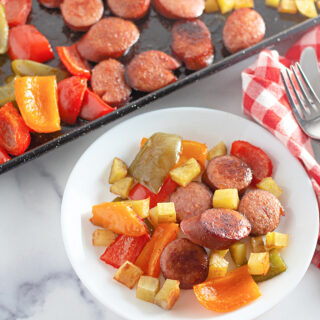 kielbasa sheet pan with peppers and potatoes in back with a plate of the kielbasa potatoes peppers in front
