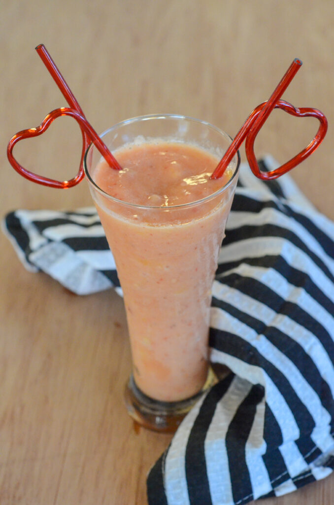dairy free tropical smoothie with orange juice and frozen fruit in a glass with two heart straws
