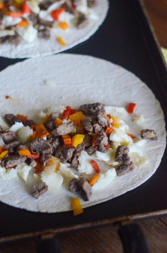 open Philly cheese steak quesadillas on black griddle 
