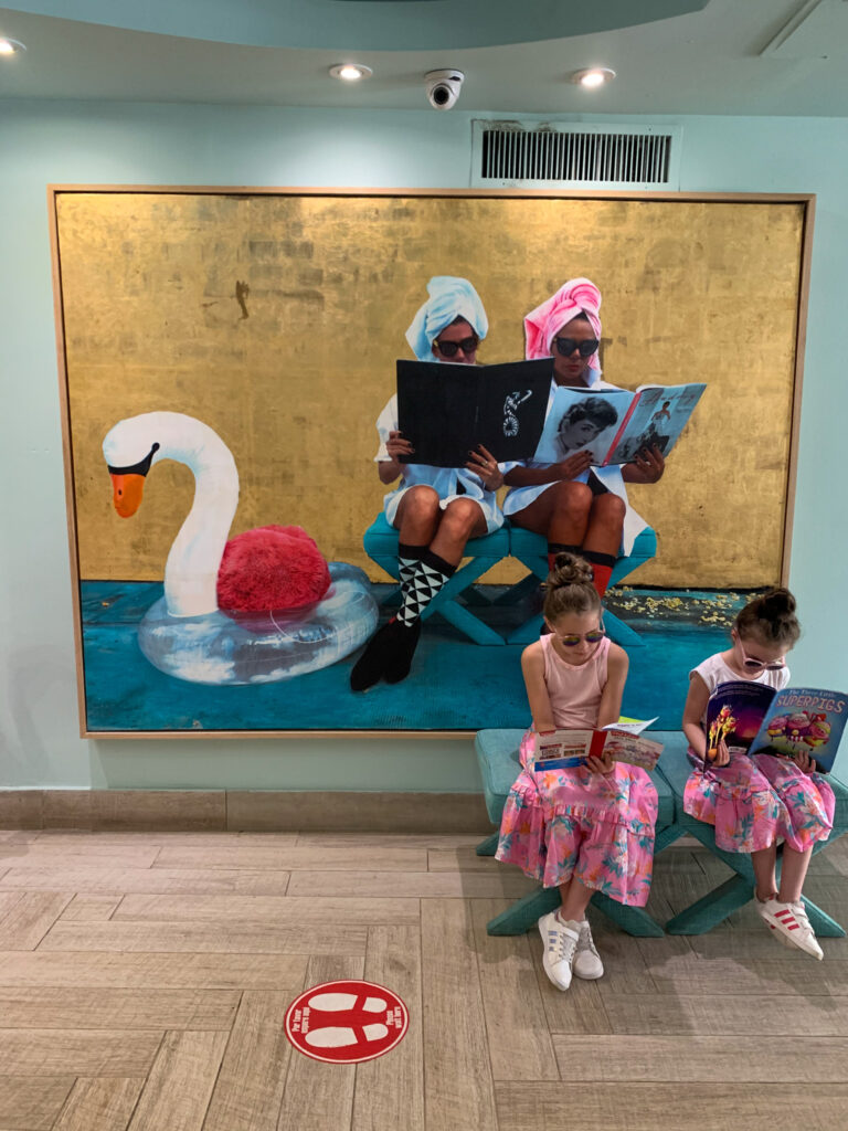 two little girls at Comfort Inn San Juan reading books mirroring the two girls in a large framed artwork behind them