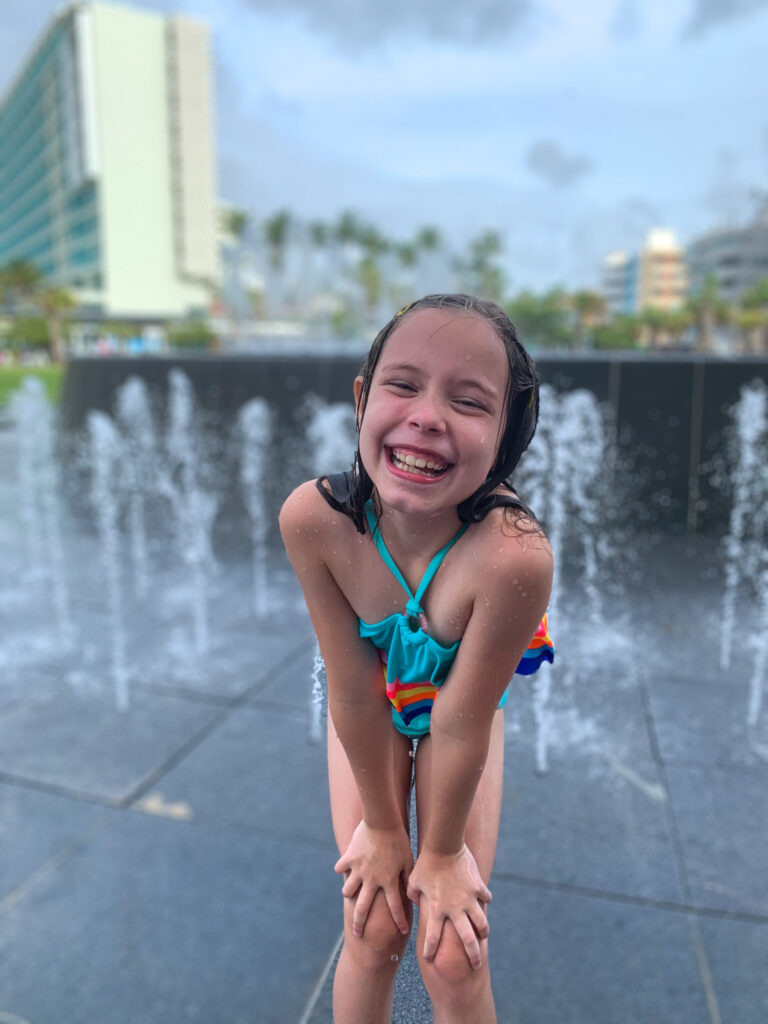 a girl smiles while playing in the splash pad at Condado Beach in San Juan Puerto Rico