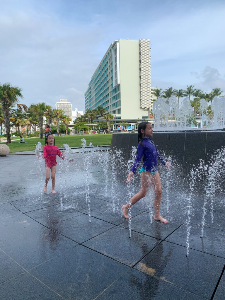 two girls running through splash fountain on Condado Beach in San Juan, Puerto Rico 