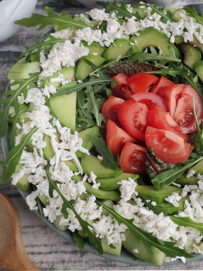 gorgeous layered spinach arugula salad with tomatoes and feta on a gray plate