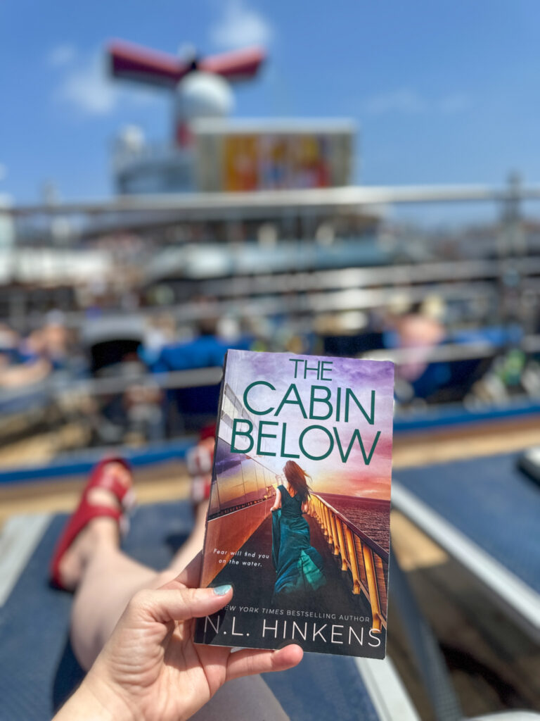 woman with cruise ship books while she lounges on Carnival Valor pool deck
