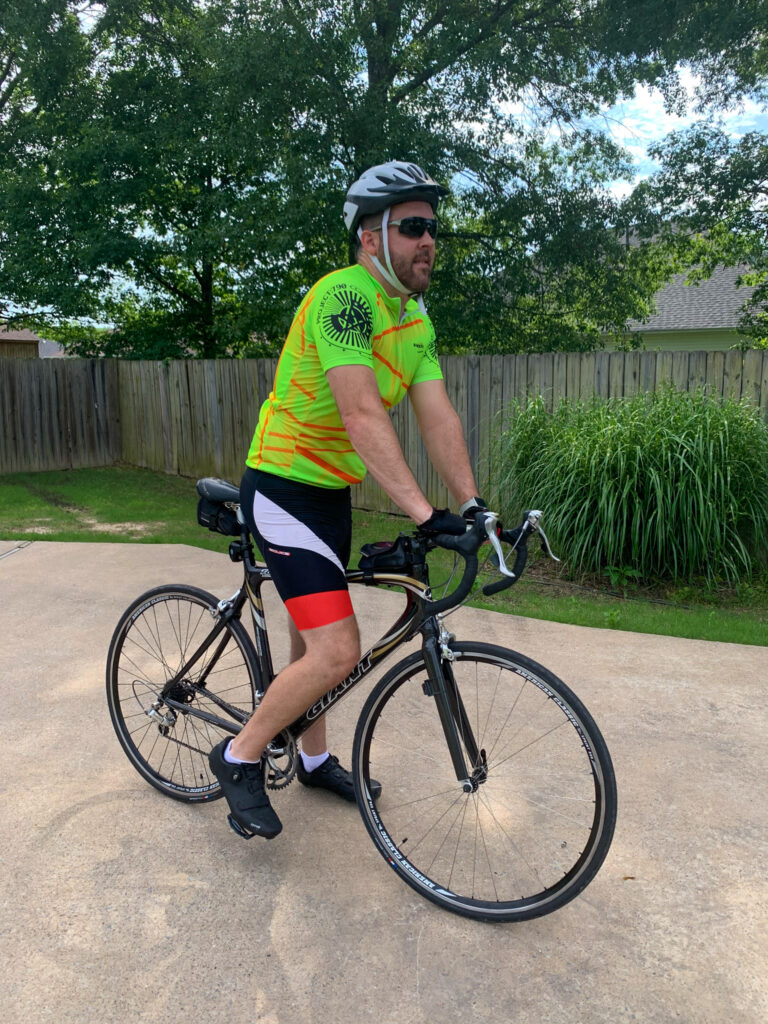 man wearing men's cycling shirt, road bike helmet, cycling gloves on a Giant ride bike