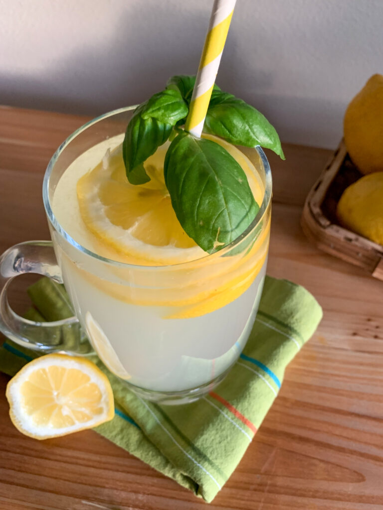 a glass mug of basil vodka lemonade with a striped straw and fresh basil on top