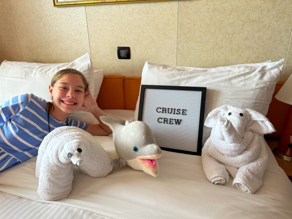 girl smiles with cruise captions on letter board among towel animals in cruise cabin
