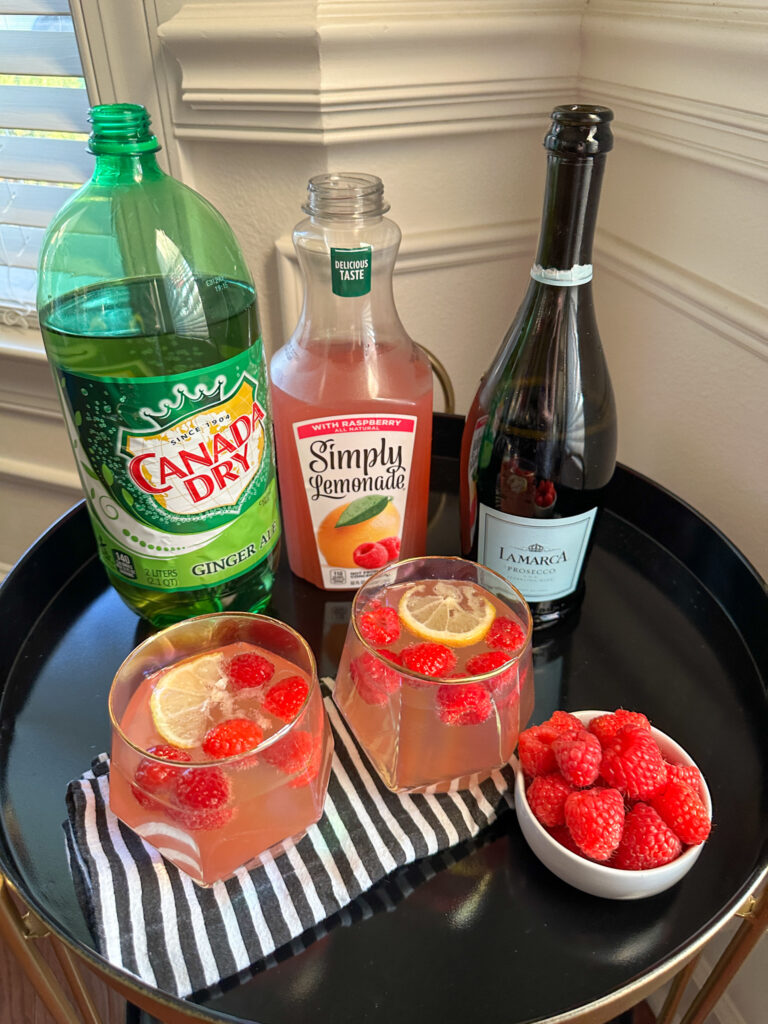 two glasses of raspberry lemonade with ginger ale and Prosecco cocktail with bottles in back