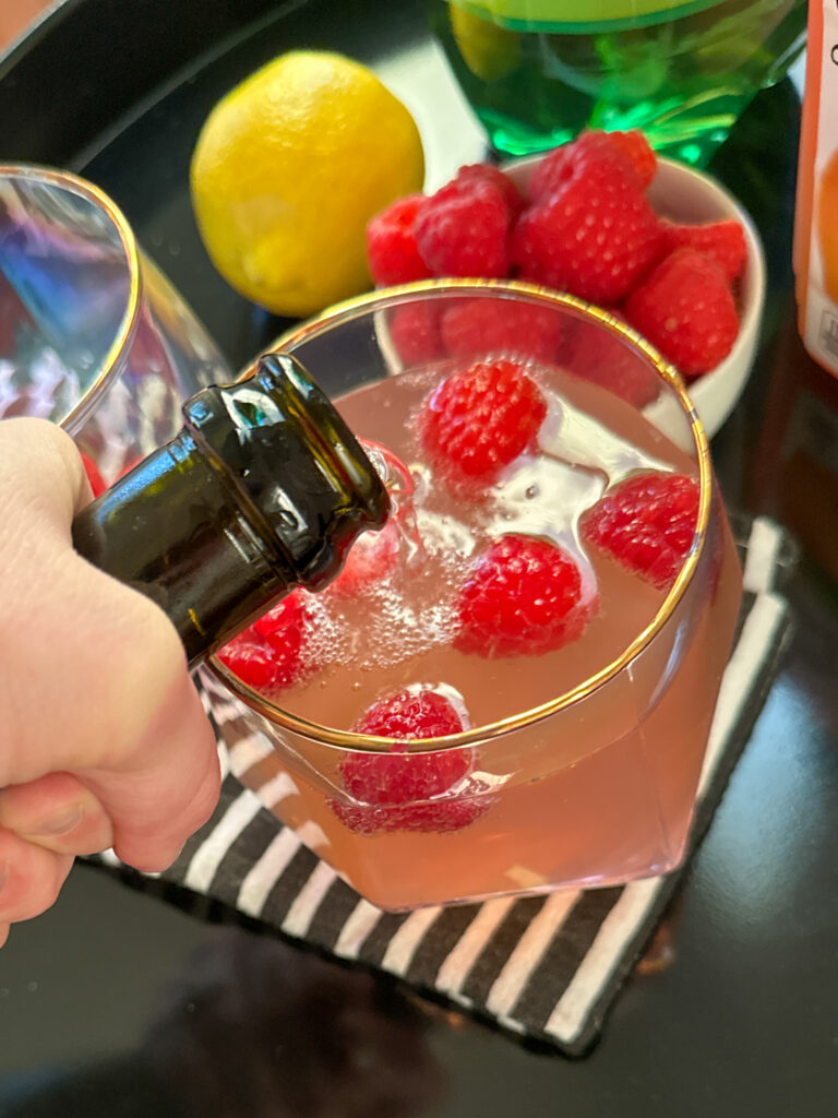 woman pours Prosecco into raspberry lemonade ginger ale cocktail