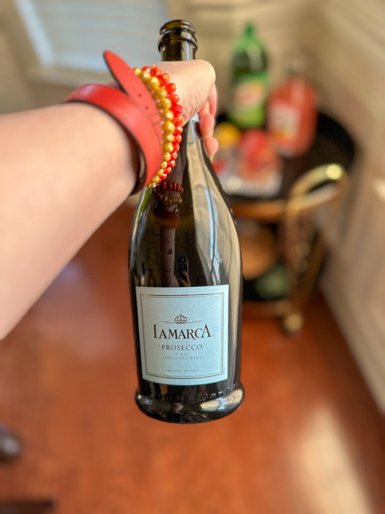 woman holds LaMarca Prosecco for cocktail with giner ale with bar cart blurred in back