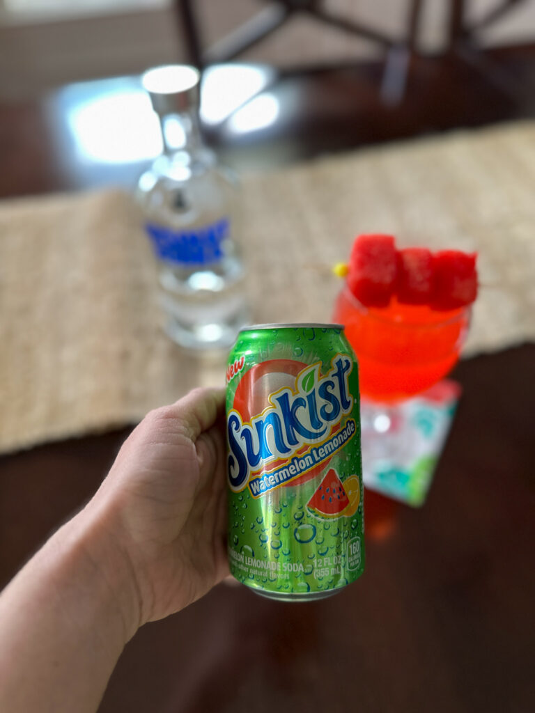 woman holds Sunkist Watermelon Lemonade with a cocktail in back