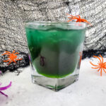 dark magic Halloween margarita with plastic spiders and cobwebs at back