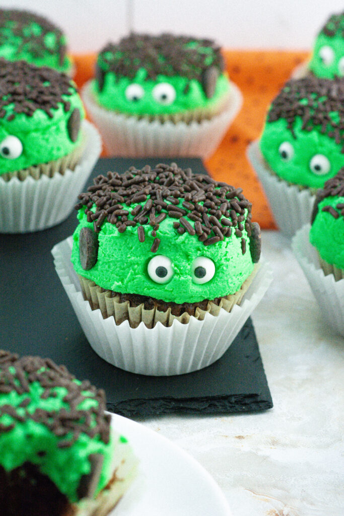 chocolate cupcakes with green icing and jimmies for Frankenstein cupcakes look on a black tray