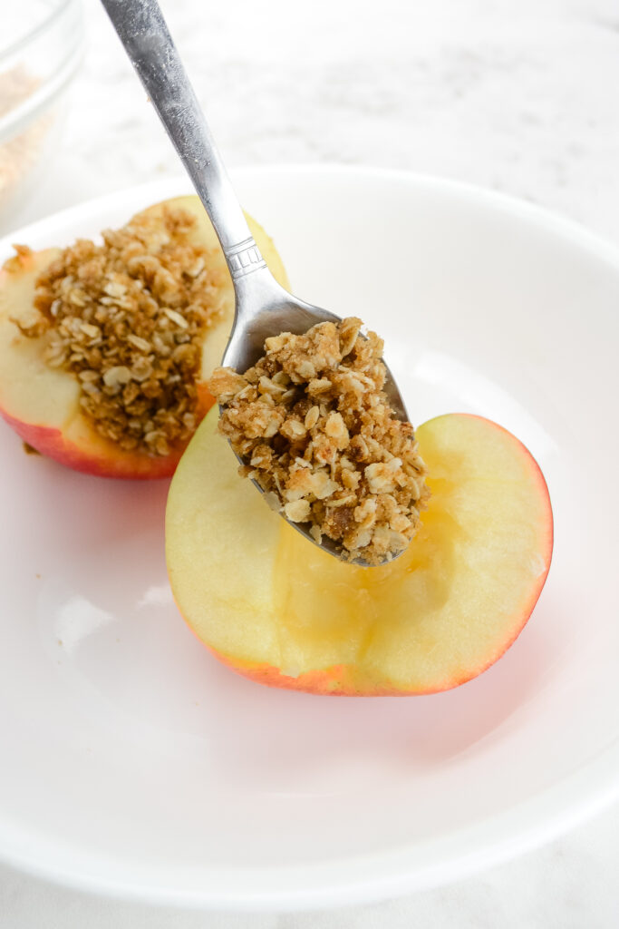dropping spoonful of oats on air fried apples on white plate