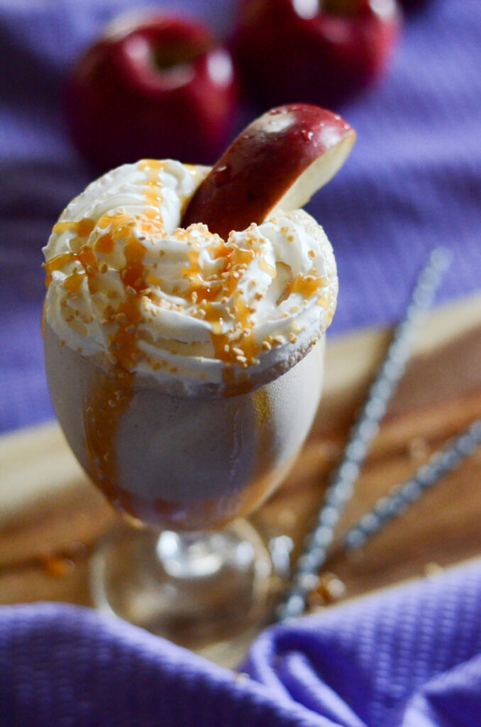 caramel apple float with an apple slice in a clear glass with purple cloth at back