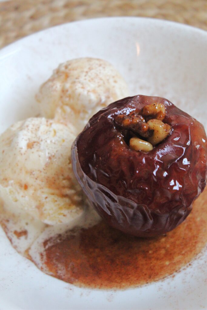 baked apple with walnuts filling and vanilla ice cream on white dish