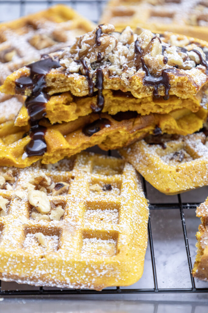 pumpkin pecan waffles with chocolate sauce stacked on wire rack