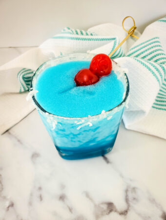 blue Christmas drink - Jack Frost holiday cocktail with rum in front of striped towel