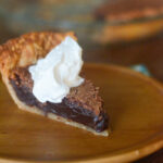 chocolate chess pie with whipped cream on wooden plate on blue napkin