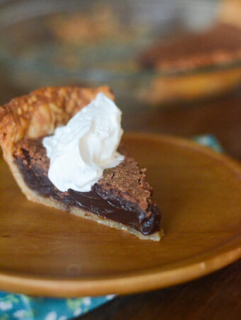 chocolate chess pie with whipped cream on wooden plate on blue napkin