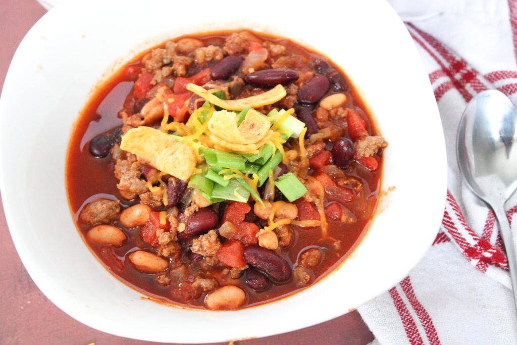 beef and sausage chili in white bowl with red and white napkin at side