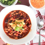 top down photo of beef and sausage chili in a white porcelain bowl with toppings
