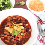 beef sausage chili in white serving bowl with condiments around