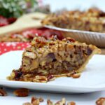 pecan salted caramel turtle pie on a white plate with pie at back