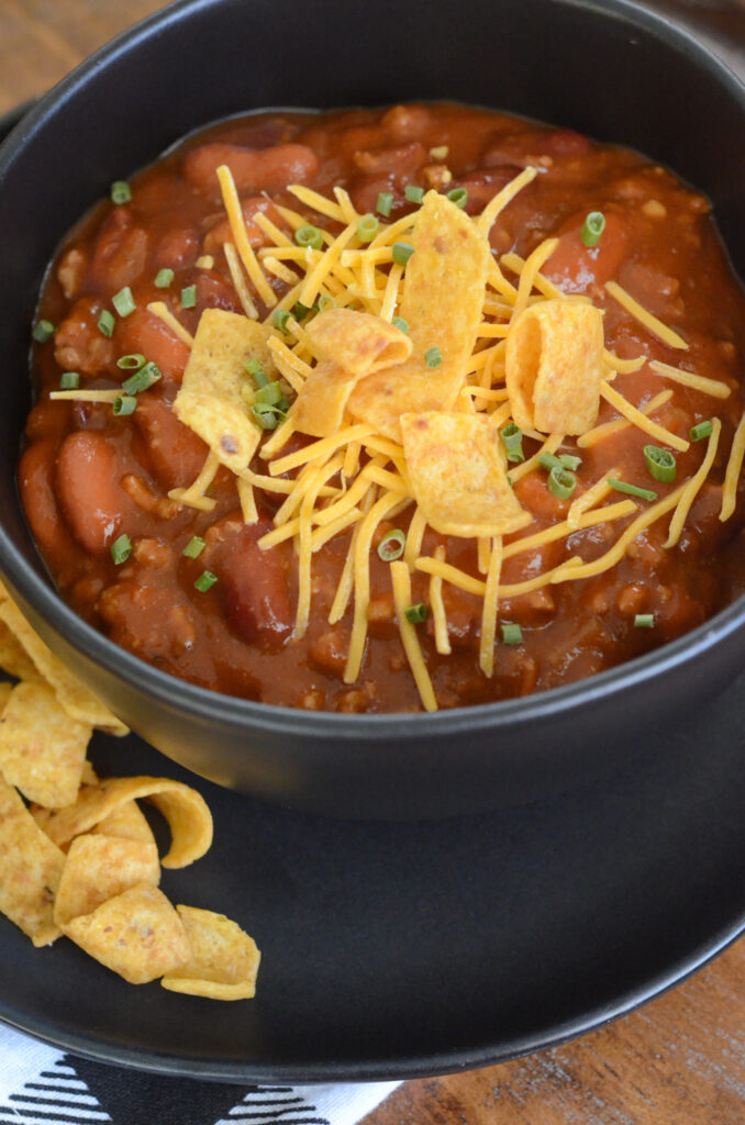 slow cooker three bean chili with beef in black bowl with toppings