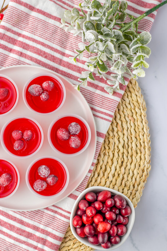 cranberry Jello shots with sugared cranberries on tray with cranberries in bowl