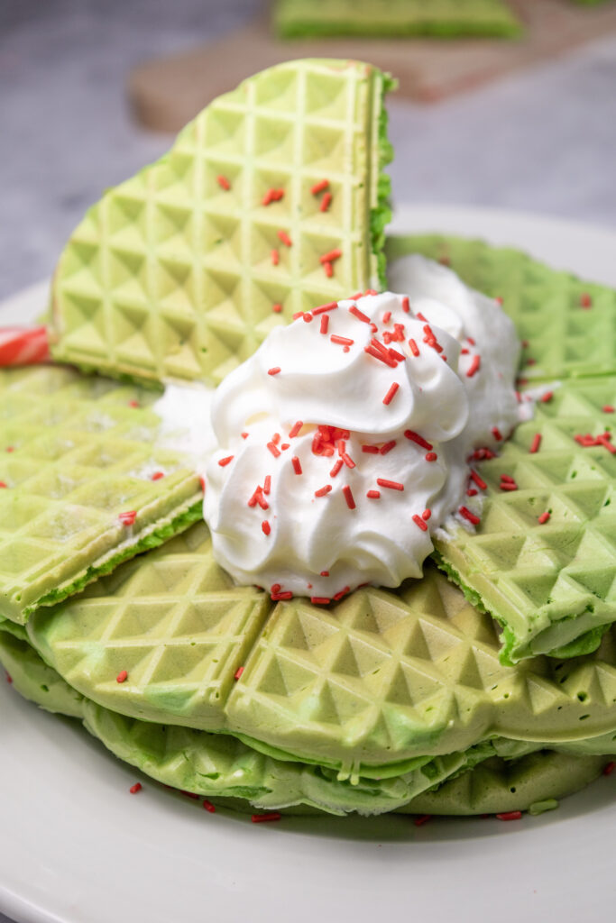 green waffles for Grinch breakfast ideas stacked on plate with whipped cream