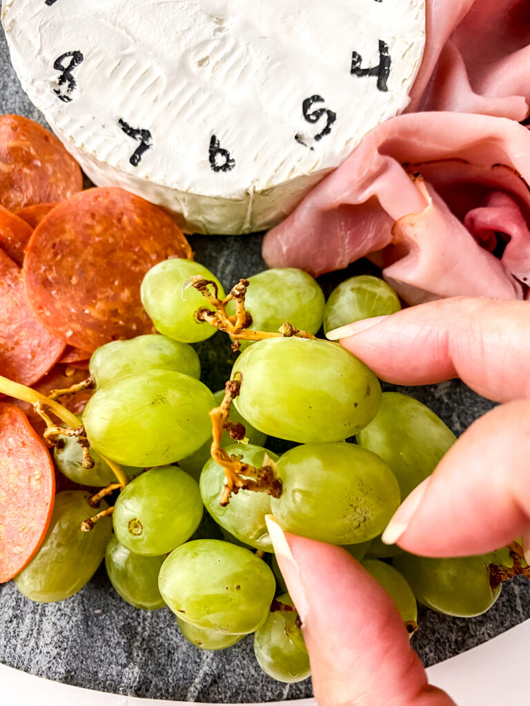 woman's hand putting grapes onto NYE charcuterie board