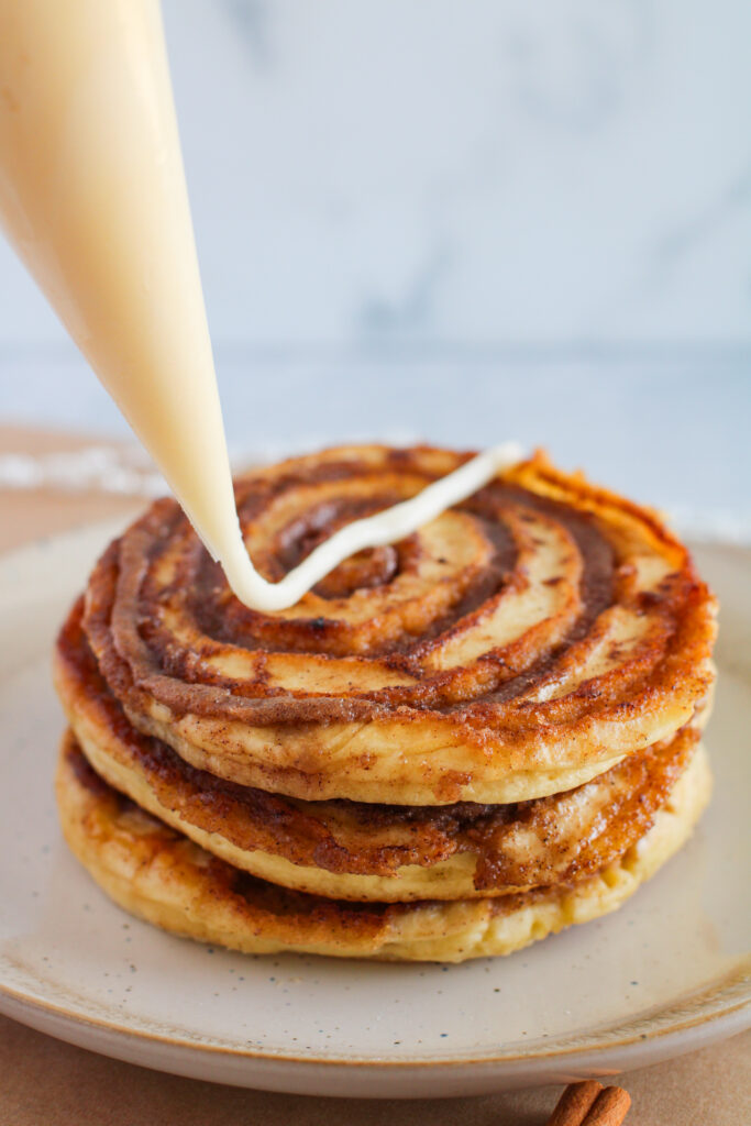 cinnamon roll pancakes with cream cheese icing being piped on for a snowflake pancake design