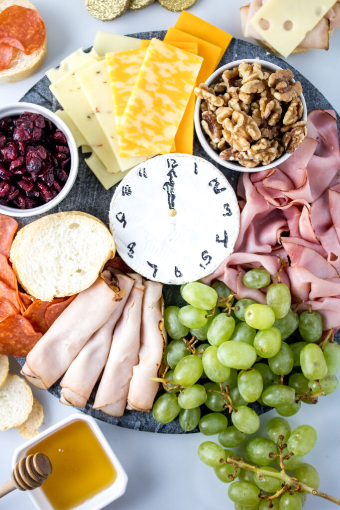 New Year's charcuterie board on white table with brie clock